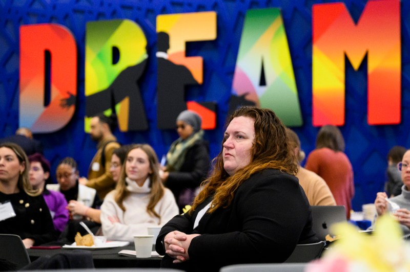 Audience members are attentive while sitting in front of a blue background with multi-colored text "Dream" displayed.