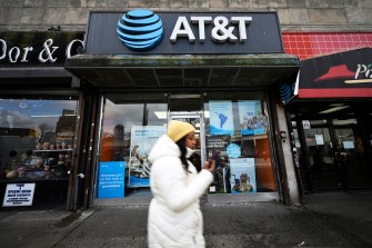 Person wearing white jacket and yellow beanie walking in front of AT&T store.