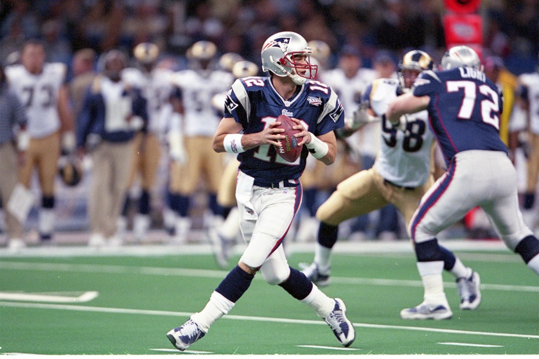 Tom Brady running while holding a football.