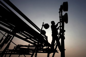 The silhouette of a person on top of a telephone tower at sunset.