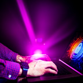 A person using a laptop in front of a purple beam of light.