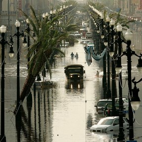 A military truck driving down a flooded street in between lampposts.