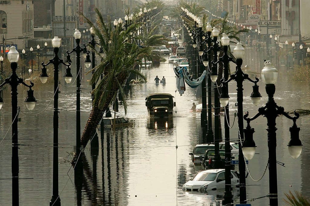 A military truck driving down a flooded street in between lampposts.