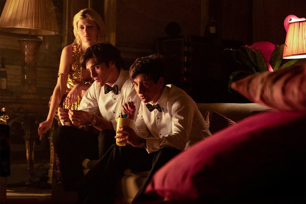 A screen capture of a scene from Saltburn with two men sitting on a couch and a woman standing behind them leaning over them.