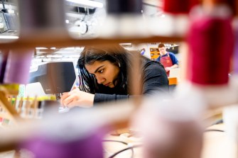 A person, viewed behind a display of multi-colored thread, uses a sewing machine.