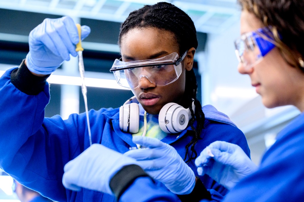 Student wearing safety goggles and headphones around their neck performing a lab experiment.