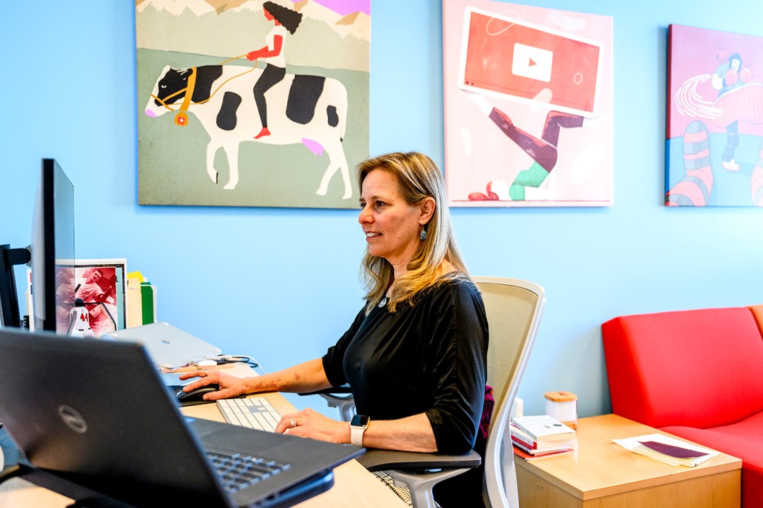 Alycia Markowski sitting at a desk in a room painted blue with colorful, whimsical paintings on the wall.