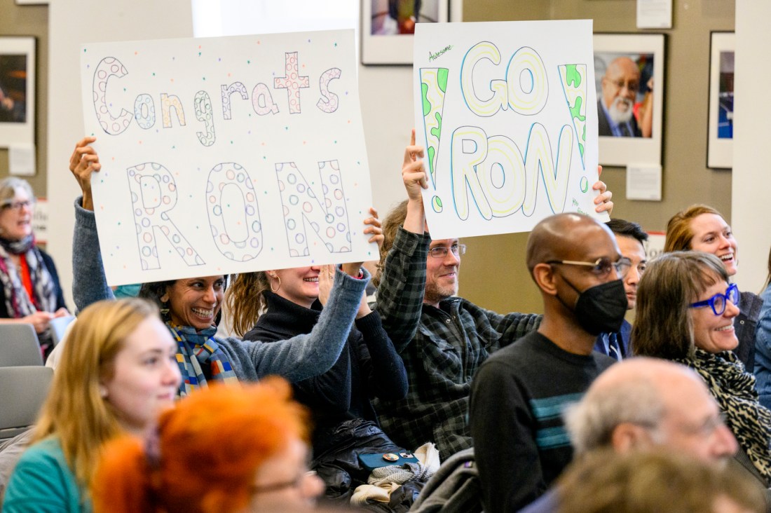 Two audience members holding up signs that say 'Congrats Ron' and 'Go Ron!' on them.