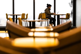A person sits working on a laptop in a brightly lit study space.