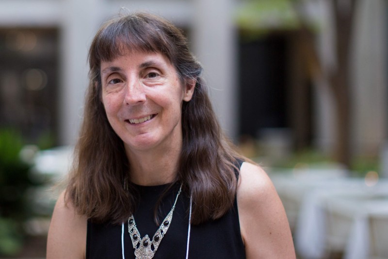 Gretchen with shoulder-length brown hair and a black shirt, smiling outside