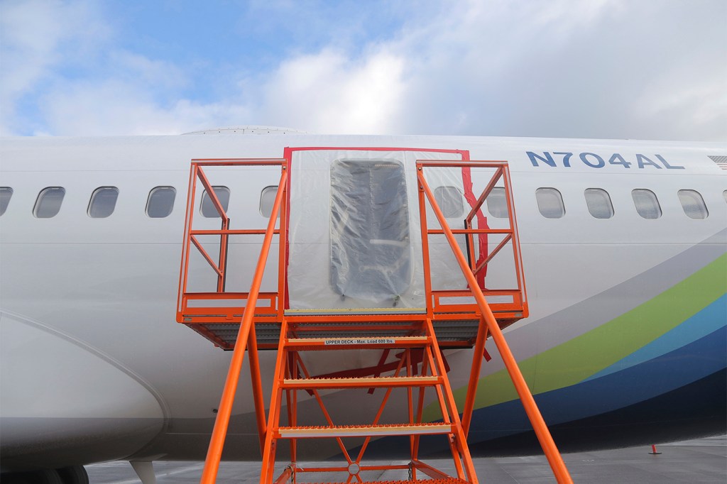 A Boeing airplane with an open area where a door might be. The area is covered with plastic and there are orange steps leading up to it.