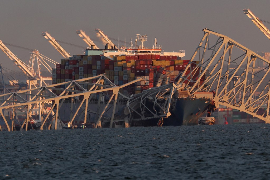 A cropped image showing a cargo ship with the bridge collapsed around it.