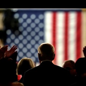 Silhouette of Joe Biden in a tunnel with an American flag on the wall in front of him.