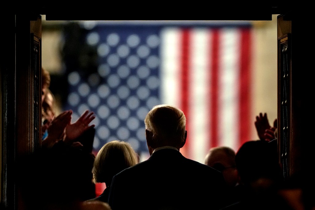 Silhouette of Joe Biden in a tunnel with an American flag on the wall in front of him.