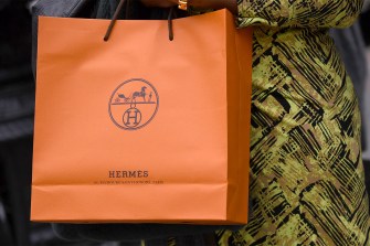 A person holding an orange retail Hermes bag.