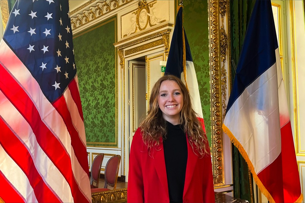 Keira O'Connor standing in between a US and French flag at the US Embassy in Paris.