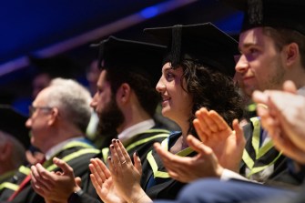 Students wearing caps and gown clapping.