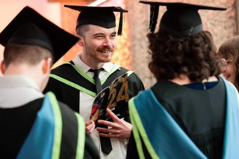 Students in caps and gowns speaking with one another.