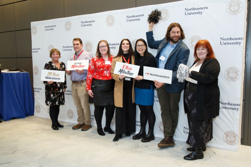 A group of 7 people posing for a photo holding signs. 