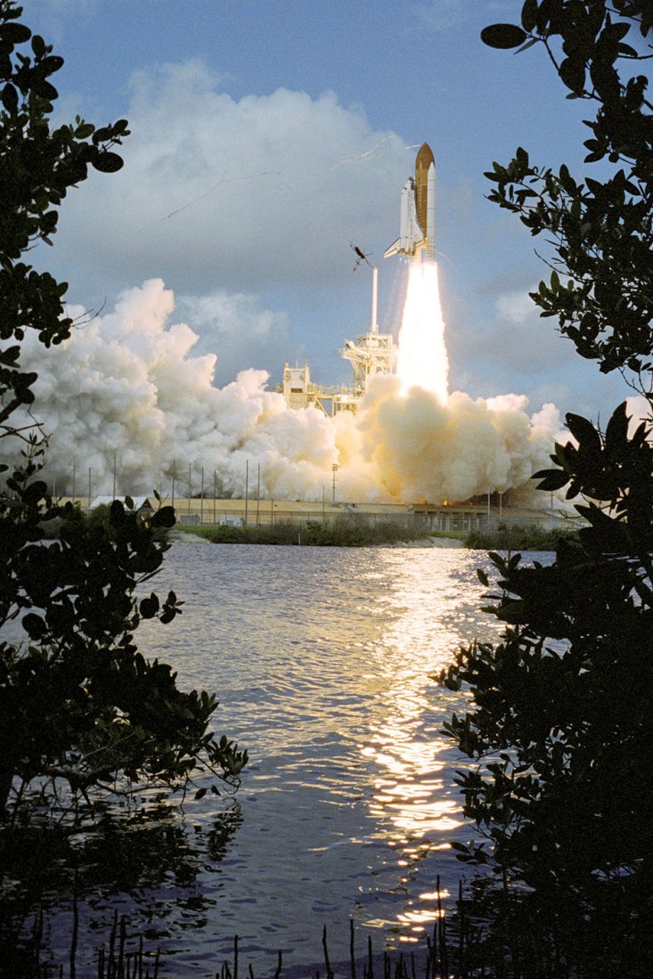 Space shuttle blasting off from a space station.