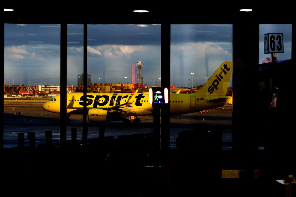 A spirit airplane on the tarmac outside of an airport.