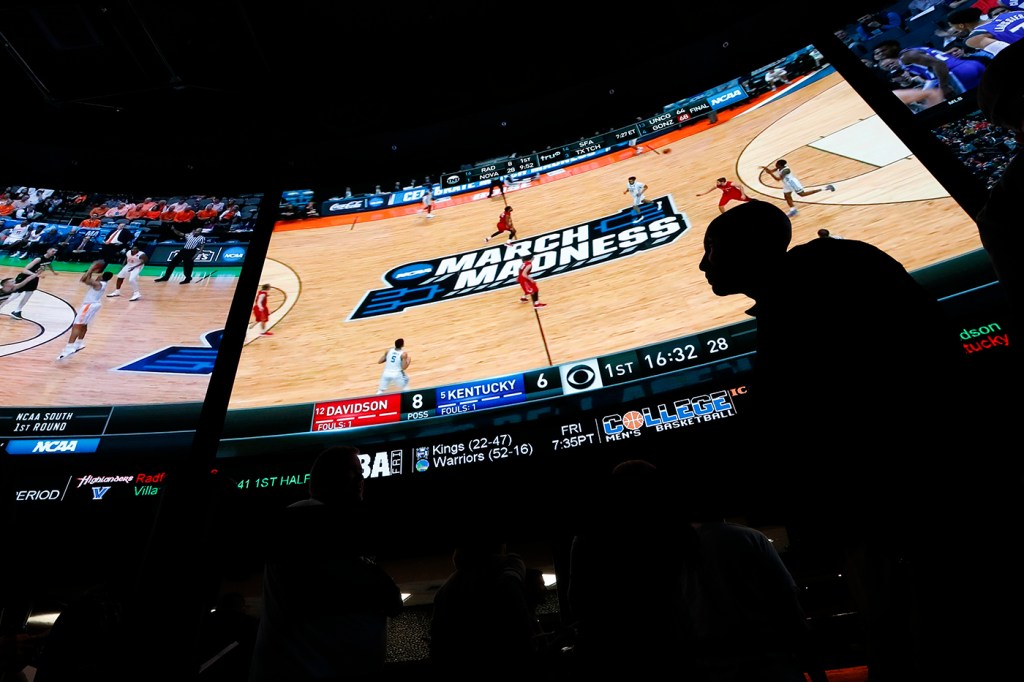 The silhouette of a person in front of a large screen airing a basketball game.