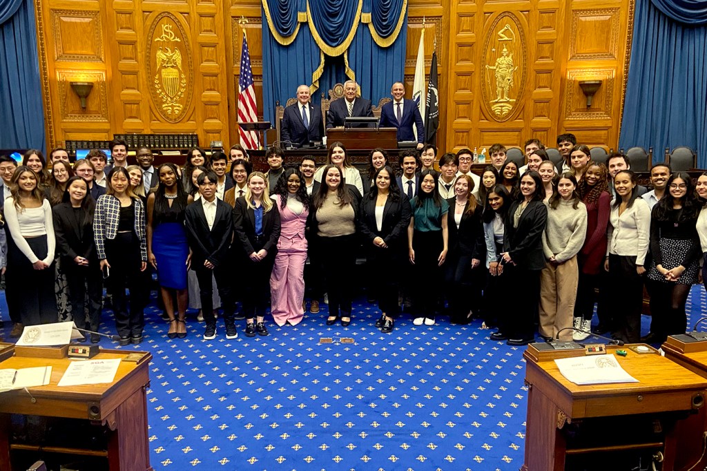 Dozens of people pose for a picture in a blue carpeted room with yellow-colored walls.