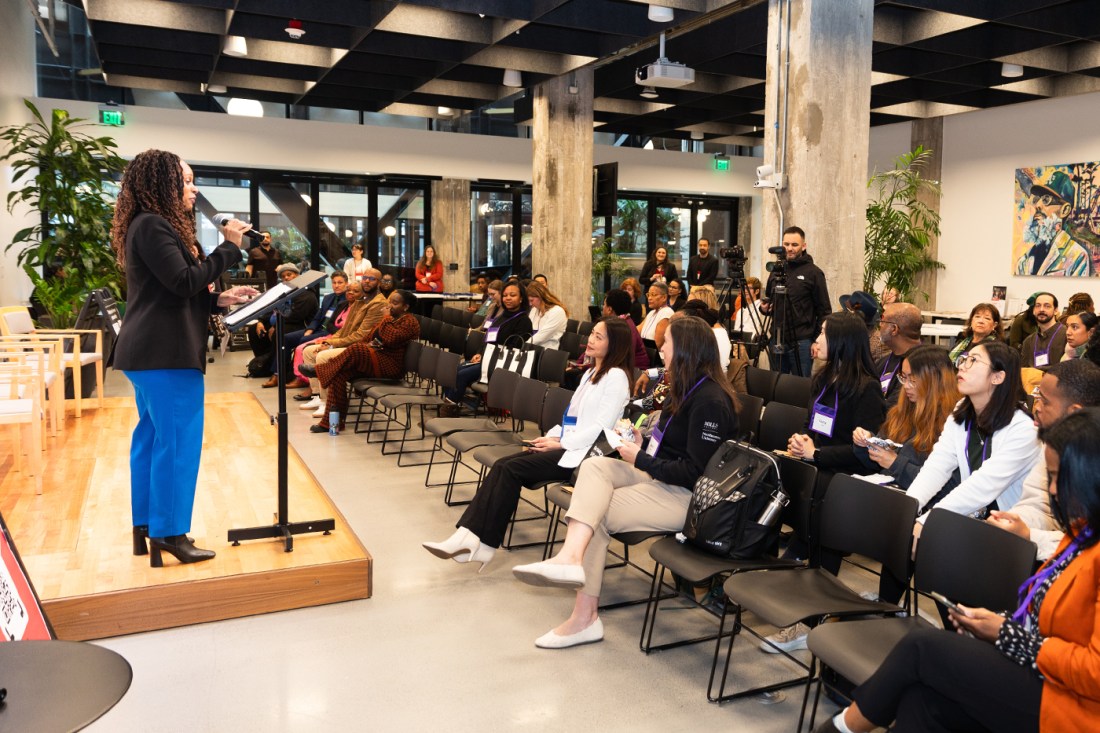 A room full of audience members sitting in chairs listening to a speaker at the front of the room.