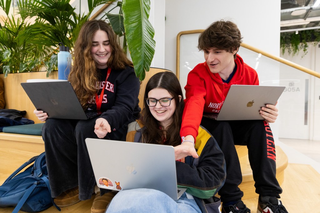 Three people sit together, working on their laptops individually.