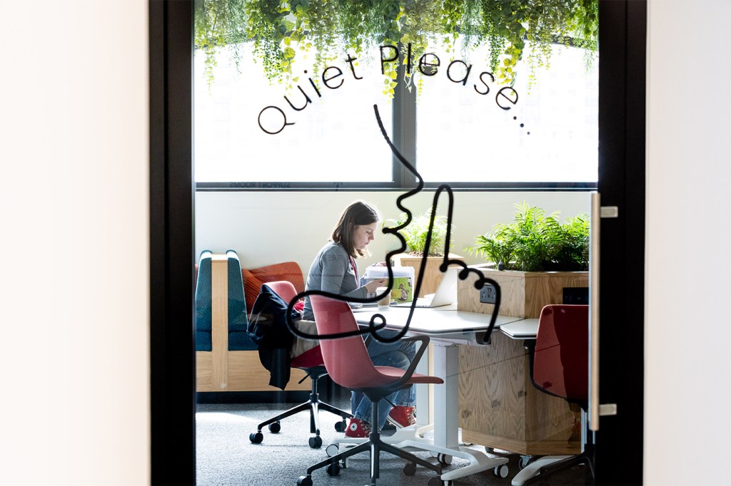 A person studies in a white-colored room surrounded by green plants.
