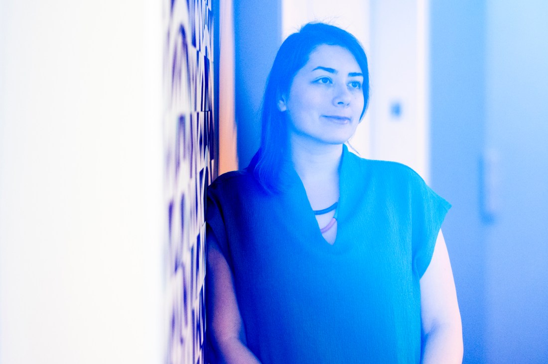 A woman poses next to a wall for a portrait, with a blue filter over the image.