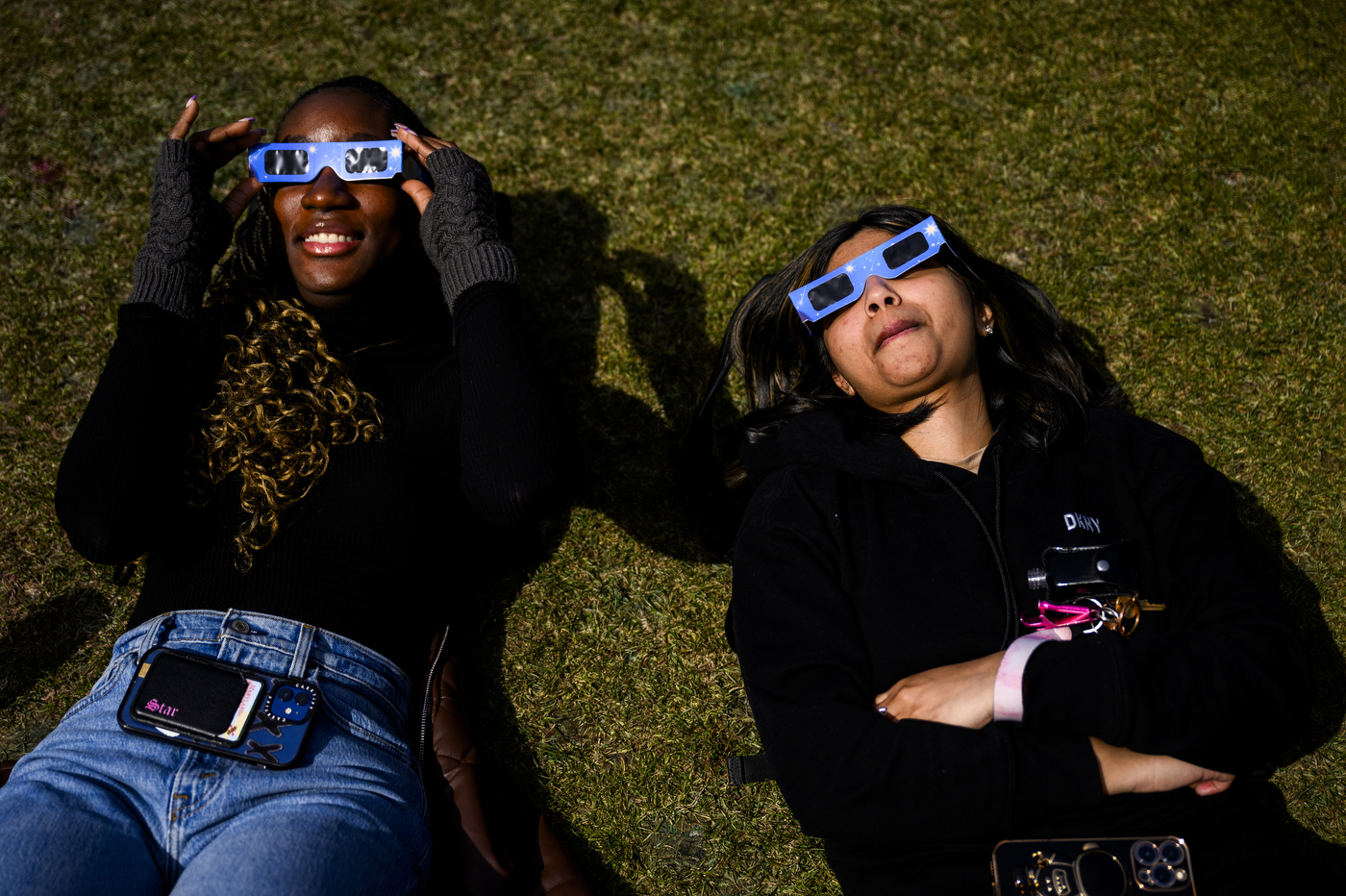 Two students laying on the grass looking up at the solar eclipse wearing eclipse glasses.