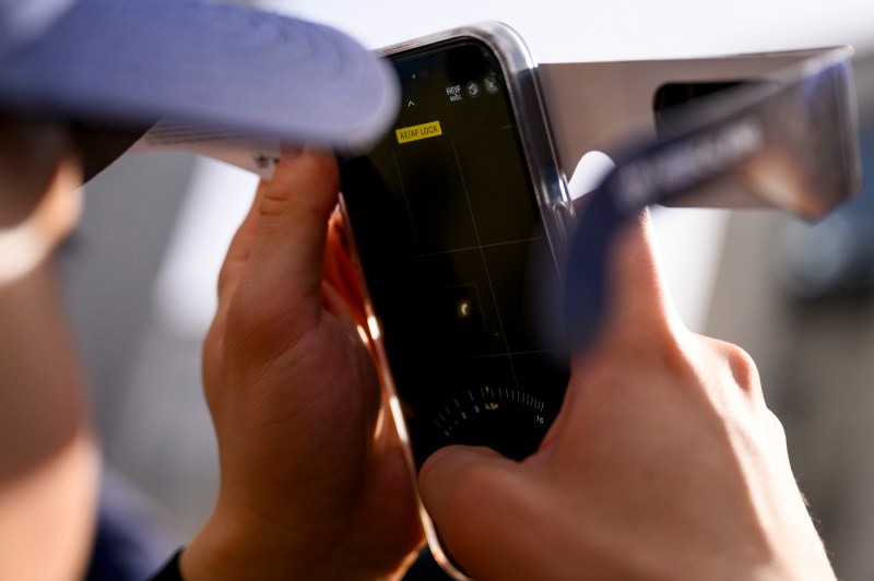 A person taking a photo of the solar eclipse on their iPhone through the lens of their solar eclipse glasses. 