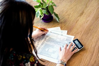 A person filling out paper tax forms using a pencil and a calculator.