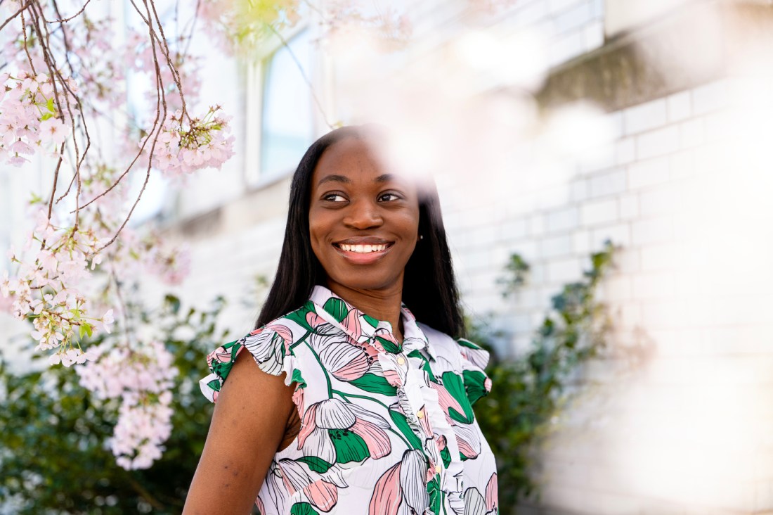 Headshot of Enam Fiattor. She is smiling and standing amongst a blooming cherry blossom tree.