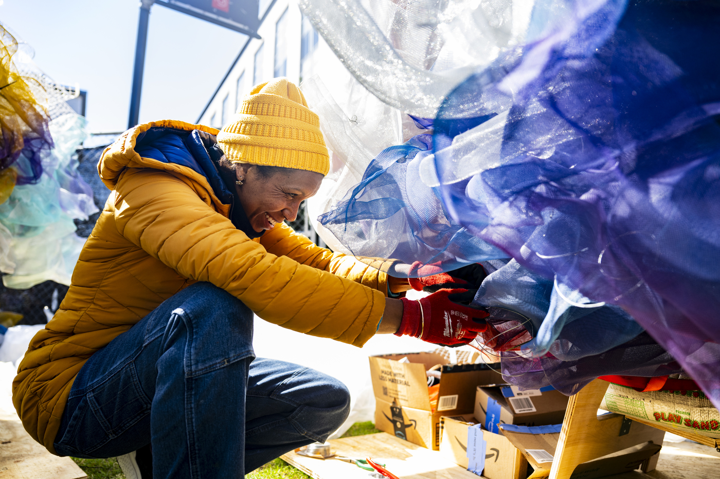 A person wearing a yellow jacket installs a purple-colored art piece on a wall.