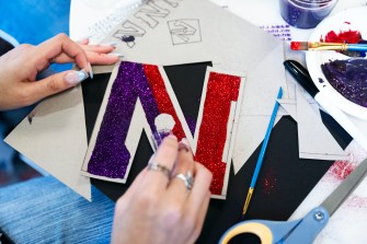 A student decorating their graduation cap with a sparkly red and purple N.