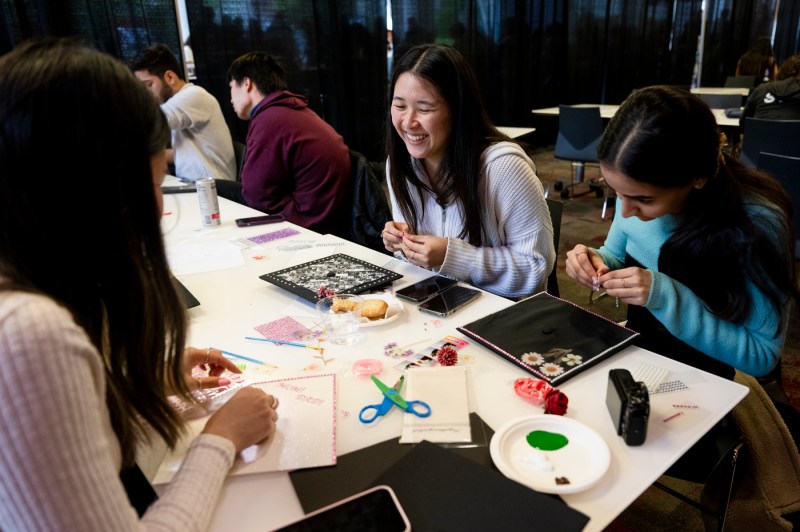 Three students sitting at a table decorating their mortarboards.