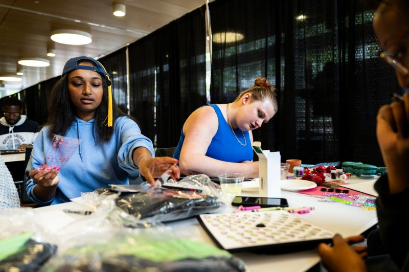 Two students sitting at a table decorating their graduation caps. 