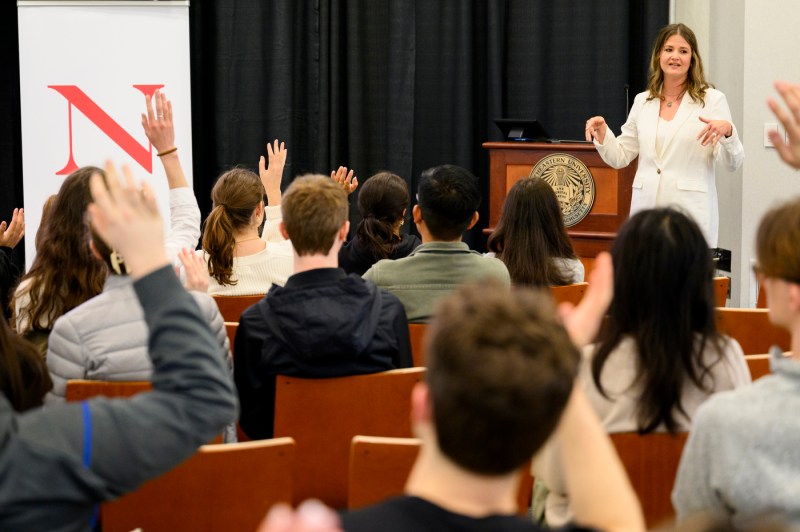 Daniele Mathras wearing a white shirt and white blazer delivering the Last Lecture in Raytheon Ampitheater.