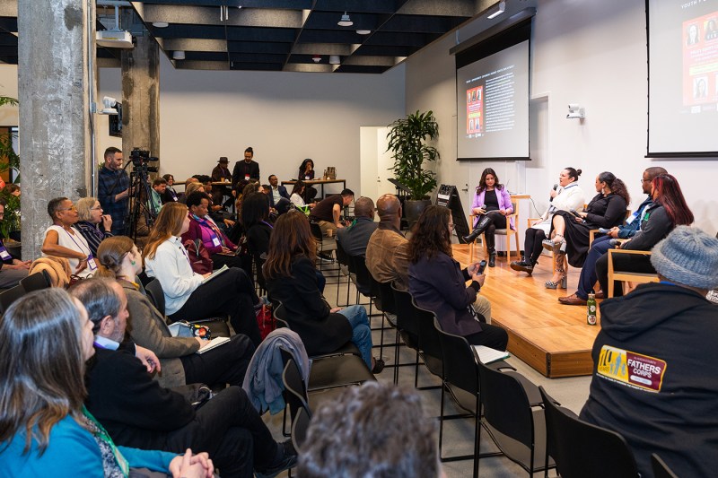 A room full of people listening to a panel of speakers.