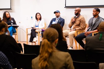 A panel of speakers sitting at the front of a room speaking into microphones.