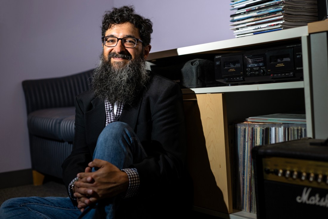 Andrew Mall, a Northeastern University music professor with short hair and glasses, sits cross-legged on a hardwood floor beside a black cassette deck and a tall stack of vinyl records. He’s surrounded by shelves packed with CDs and books. Mall says cassettes never “really died out,” despite falling out of the mainstream.