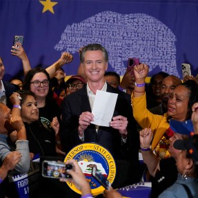 Gavin Newsom holding up a piece of paper and smiling.