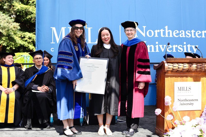 Three people wearing regalia pose for a picture on a stage near a podium.