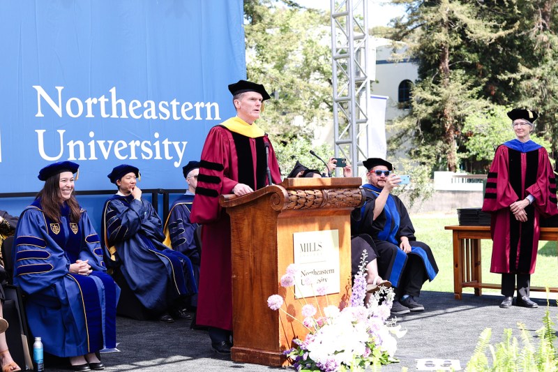 A person wearing regalia speaks at a podium at Northeastern's Oakland commencement. 