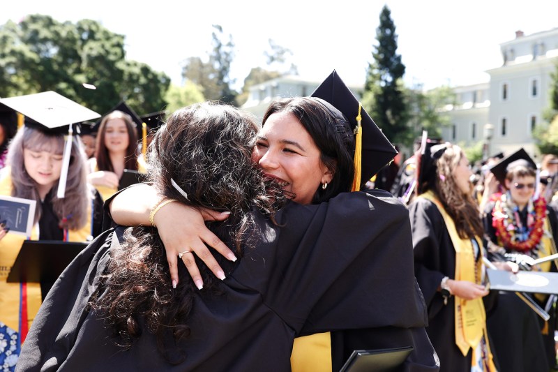 Two graduates hug each other at Northeastern's Oakland commencement.