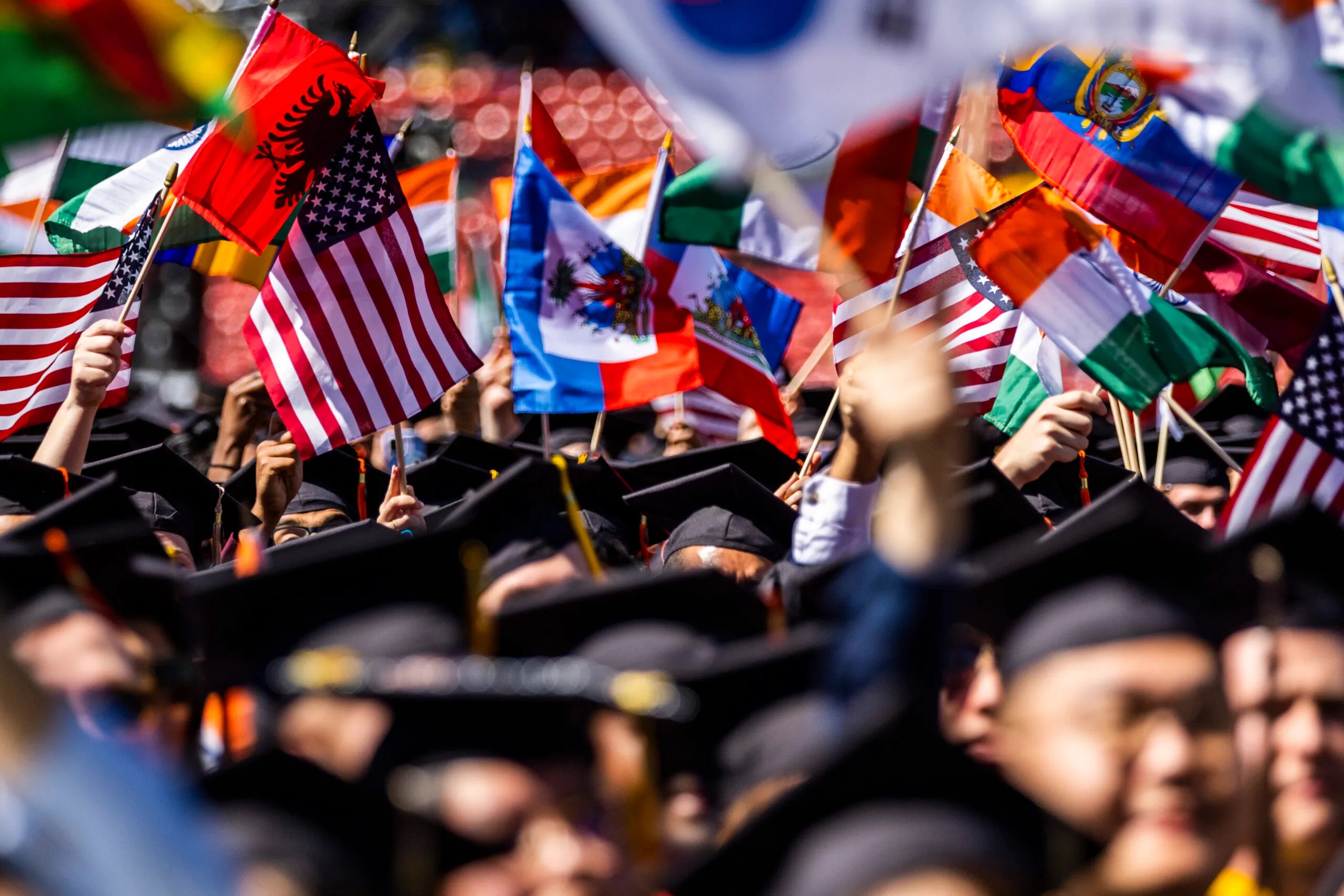 Caps and gowns at Northeastern's commencement with lots of graduates waving flags as well