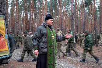 A Russian Orthodox Church priest gesturing while speaking to soldiers outside.