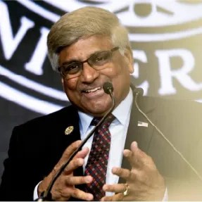 Sethuraman Panchanathan smiling while speaking on a podium in front of the Northeastern University seal.